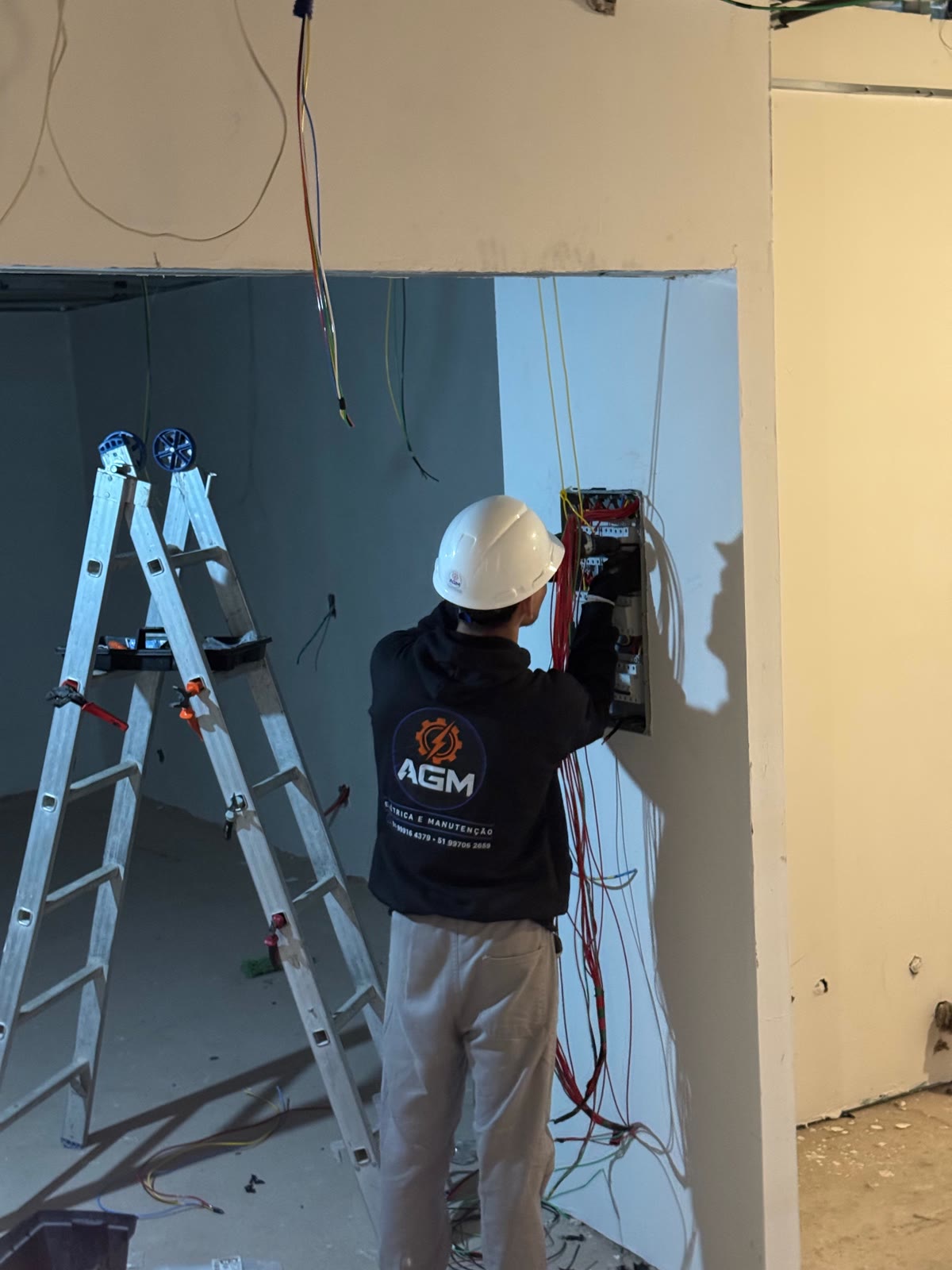 Profissional da AGM com capacete executando instalação em quadro elétrico